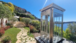 Un moderno pabellón de vidrio con un sendero de piedra que conduce a una terraza con vista a una masa de agua.