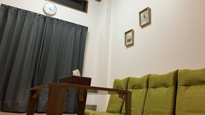 Una sala de estar con un sofá verde, una mesa de madera, un reloj en la pared y una ventana con cortinas.