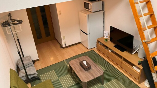 Un espacio habitable compacto con kitchenette, televisor, una mesita y un tapete verde a rayas.