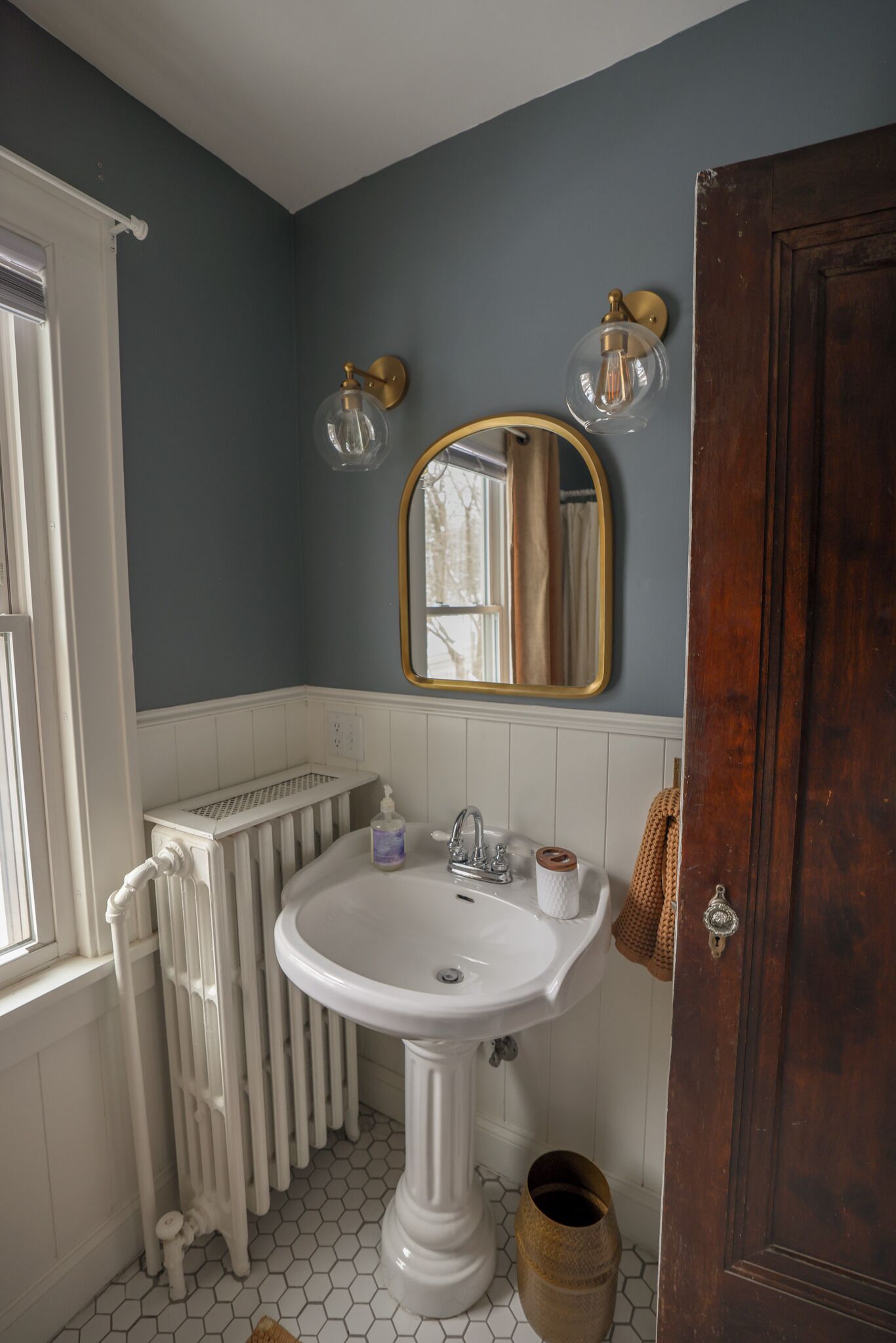 A bathroom with a white pedestal sink, a mirror with a gold frame, and a radiator.