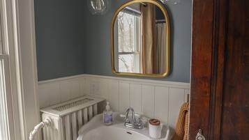 A bathroom with a white pedestal sink, a mirror with a gold frame, and a radiator.