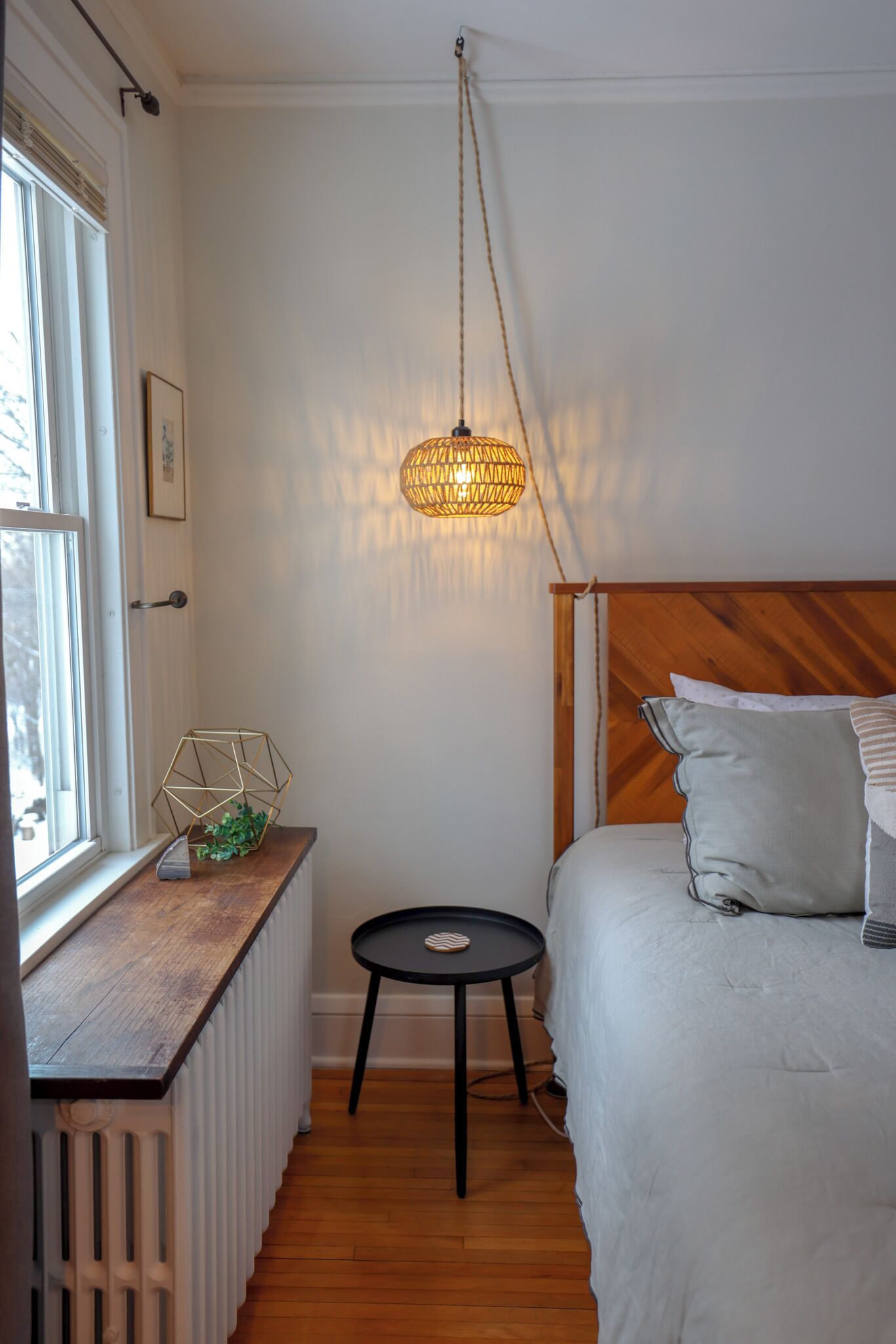 Ein Schlafzimmer mit einem Holz-Kopfteil, einem Nachttisch, einer Pendelleuchte und einer Heizung.