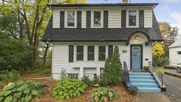 A two-story house with a front porch, a small front yard with plants, and a blue door.