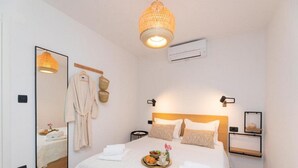 A hotel room with a large bed, a bedside table, a mirror, a hanging light fixture, and a wall-mounted air conditioner.