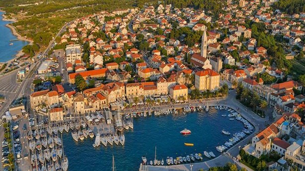 An aerial view of a coastal town with a marina filled with boats, surrounded by densely packed buildings with red roofs. - Apartment Marijana (Supetar)