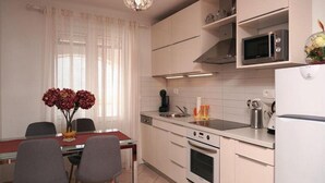 A modern kitchen with white cabinets, a built-in oven, a microwave, and a dining area with a table and chairs. - Apartment Marijana (Supetar)