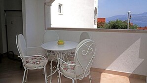 A balcony with a white table and four chairs, a view of a building, and a clear sky. - Apartment Marijana (Supetar)