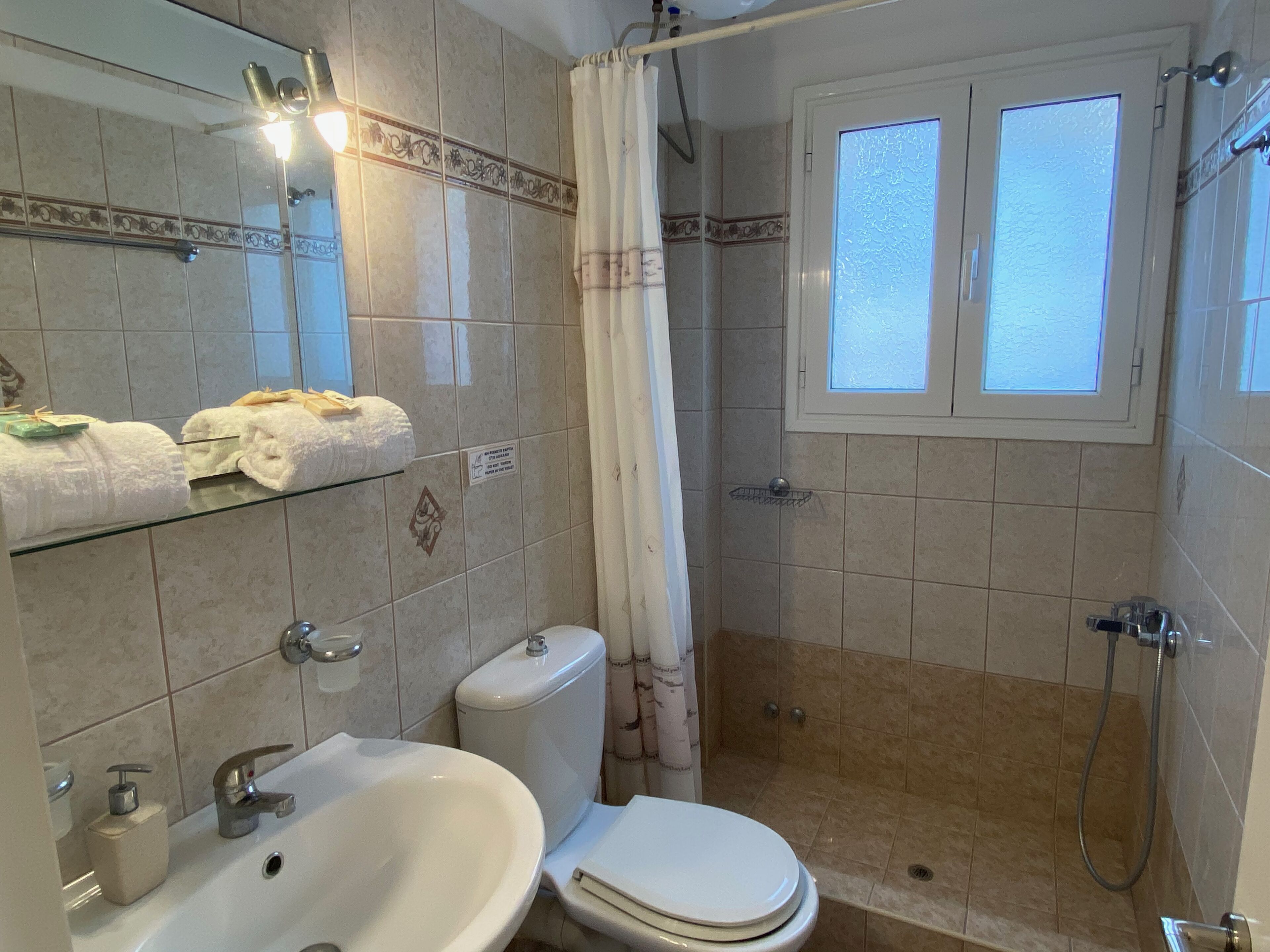 A bathroom with a sink, toilet, shower, and a window.