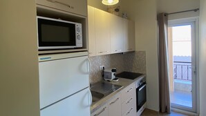 Eine kleine Küche mit Mikrowelle, Kaffeemaschine und Toaster. Eine Schiebetür führt zu einem Balkon.