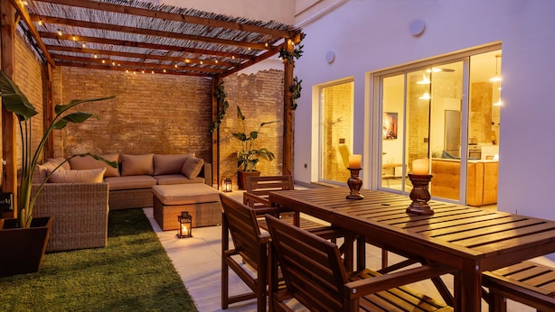 A cozy outdoor patio with a wooden table and chairs, a cushioned sofa, and a pergola with string lights. - Stylish Boutique Design Apartment Central Location with Terrace (València)