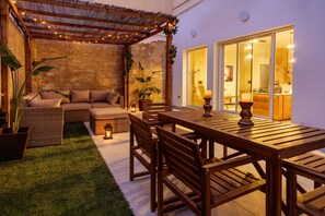 Une terrasse extérieure accueillante, avec une table et des chaises en bois, un canapé confortable et une pergola illuminée de guirlandes lumineuses.
