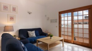 Una sala de estar con un sofá azul oscuro, una mesa de centro de madera y un gran ventanal corredero que da a un espacio exterior.