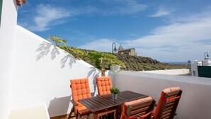 Una terraza con una mesa y sillas, una planta en maceta y vistas a una colina con una estructura al fondo.