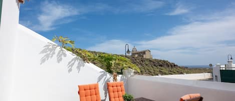 A terrace with a table and chairs, a potted plant, and a view of a hill with a structure in the distance.
