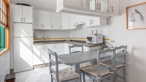 Una cocina con armarios blancos, encimera de granito, una mesa de comedor con sillas y un microondas.