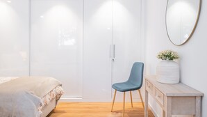 A bedroom with a bed, a chair, a wardrobe, a dresser, and a mirror.