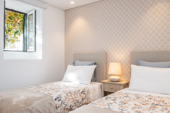 A hotel room with two beds, a window with a view of greenery, and a patterned wall.