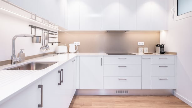 A modern kitchen with white cabinets, stainless steel appliances, and a wooden floor.