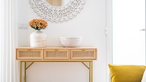 A white console table with a white vase and bowl, a decorative mirror, and a yellow cushion.