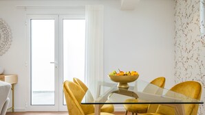 A dining area with a glass table and yellow chairs, a bowl of fruit on the table, and a door leading outside.