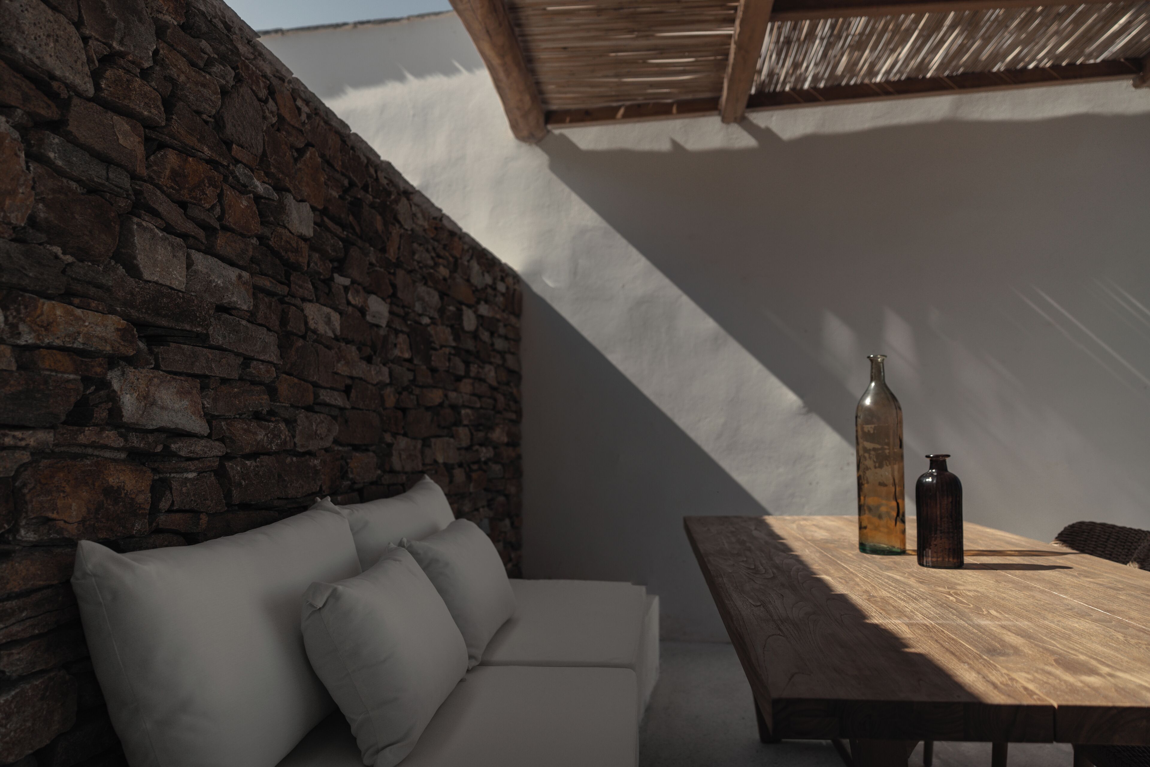 A cozy outdoor seating area with a stone wall, a wooden table, and two bottles.