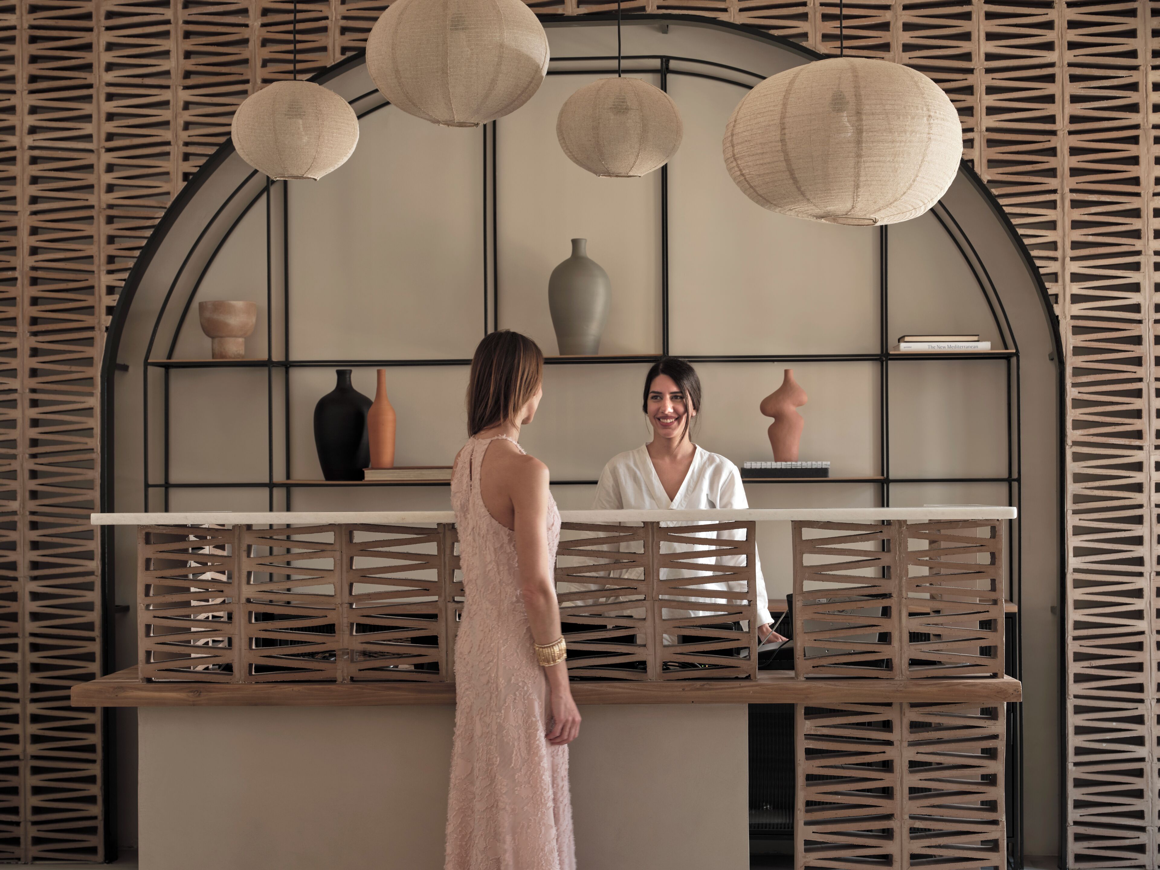 A reception area with a modern design, featuring a wooden reception desk, a white vase, and a shelf with books and decorative items.