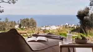 A cozy outdoor seating area with a view of the sea, a book, and a bowl of fruit. - Stamna Sifnos, a member of Design Hotels (Sifnos)
