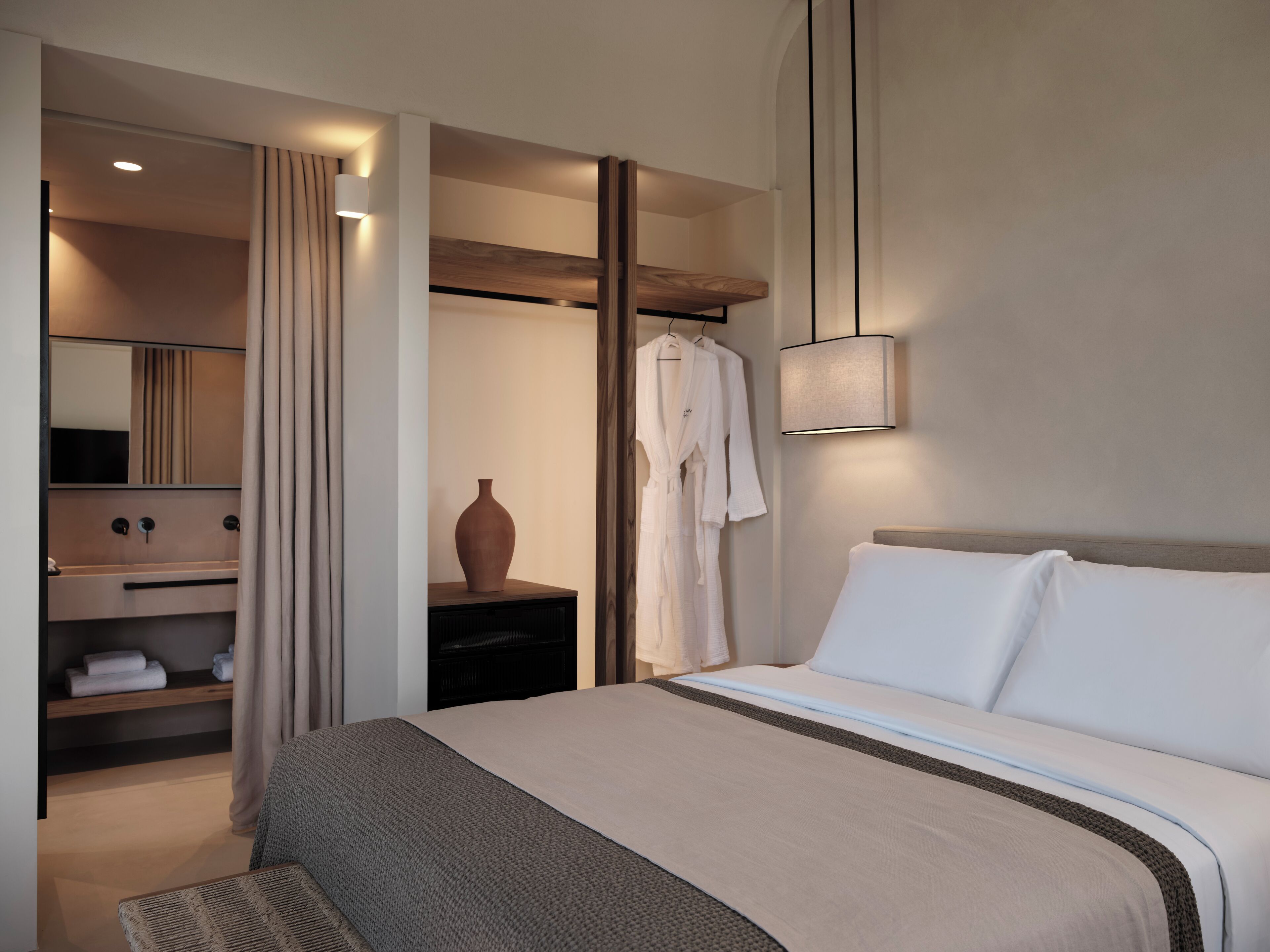 Ein modernes Hotelzimmer mit einem großen Bett, einem Nachttisch, einem Spiegel, einem Bademantel und einer Vase.