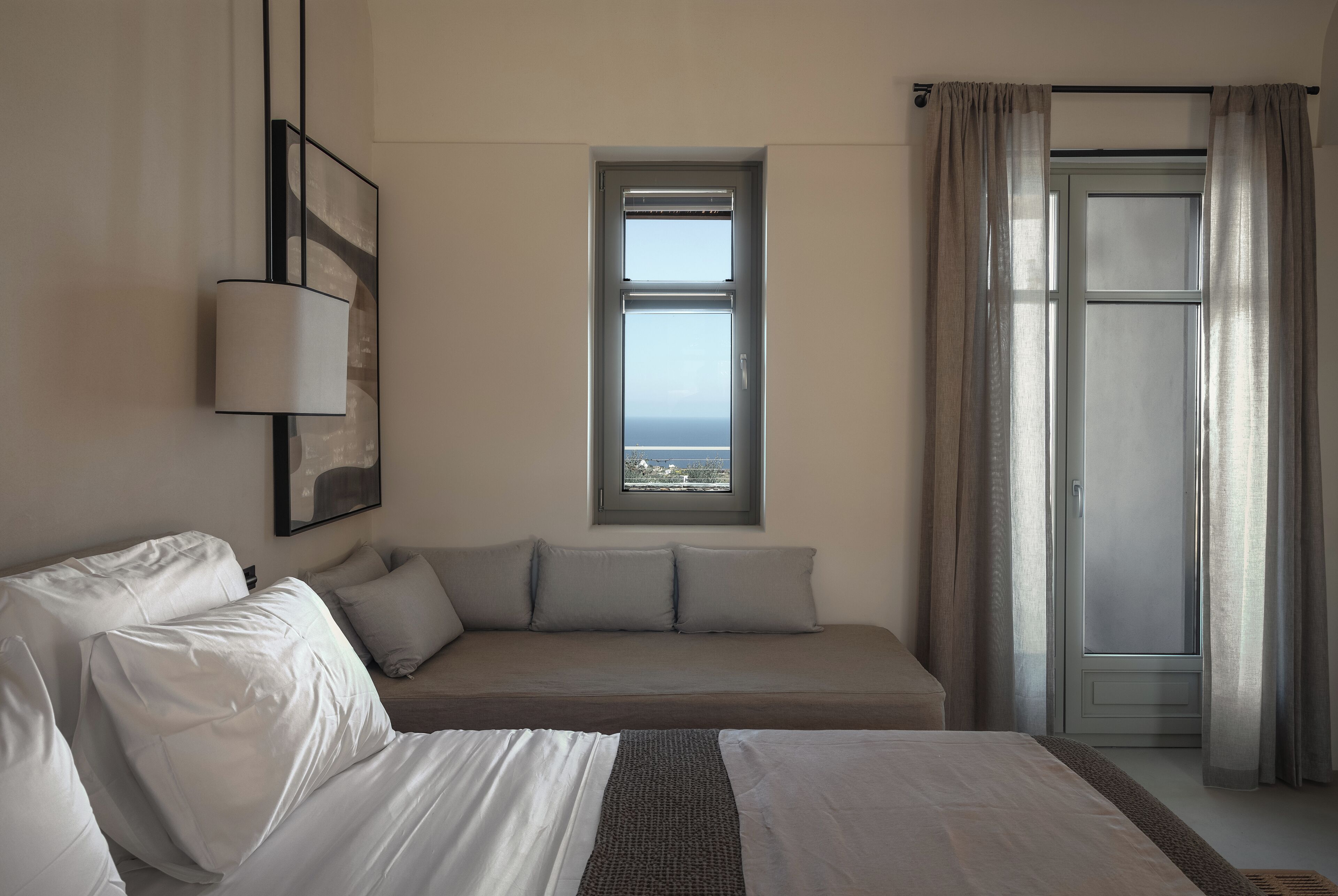 A bedroom with a bed, a sofa, a window with a view, and a door with curtains.