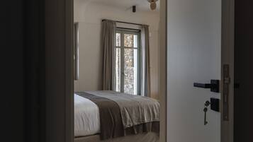 A bedroom with a bed, a window with curtains, a ceiling fan, and a door with a key in the lock.