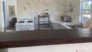 A kitchen with a gas stove, a microwave, a sink, and a blender on a shelf. - The Cottage at Lowry Hill (Christiansted)