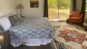 A bedroom with a bed, a chair, a lamp, and a large window. - The Cottage at Lowry Hill (Christiansted)