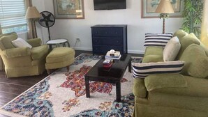 A living room with two green armchairs, a black coffee table, a blue cabinet, and a patterned rug. - The Cottage at Lowry Hill (Christiansted)