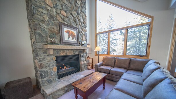 A cozy living room with a stone fireplace, a large window, and a comfortable sofa. - Walk to ski slopes! Private hot tub and garage! (Keystone)