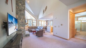 A spacious living room with a stone pillar, a large flat-screen TV, a sofa, and a dining area. - Walk to ski slopes! Private hot tub and garage! (Keystone)