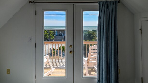 A room with a view of the ocean through a sliding door, a balcony with a chair, and a wooden deck. - Ocean-View Retreat, Sleep 8, 6-Minute Walk to Restaurants, Pet friendly (Surf City)