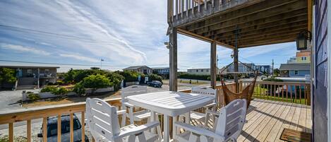 A wooden deck with a table and chairs, overlooking a street with houses and a parked car.