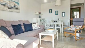 En moderne stue med sofa, sofabord og lænestol. Der er et spisebord med stole, en lampe og et billede på væggen.