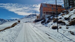 A snow-covered road leading to a wooden building with multiple windows and a balcony, surrounded by mountains and a clear sky. - Habitamar El Colorado (Lo Barnechea)