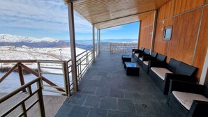 A covered outdoor seating area with stone flooring, wooden walls, and a view of snow-covered mountains. - Habitamar El Colorado (Lo Barnechea)