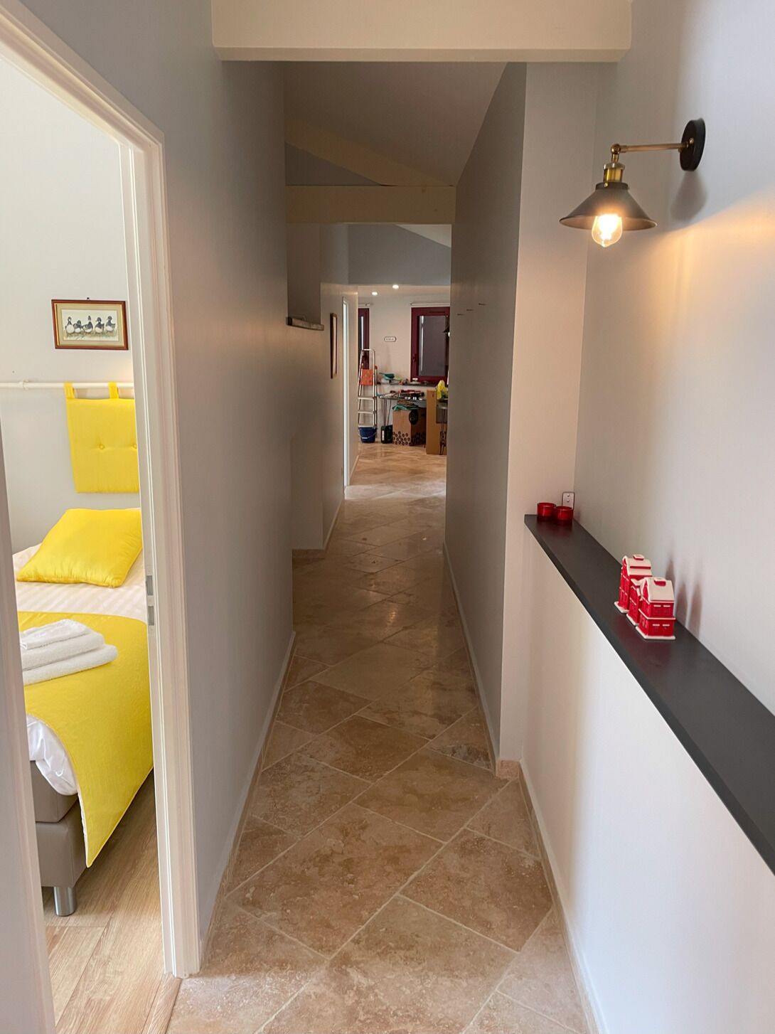 Un pasillo de hotel con una cama a la izquierda, una cocina al fondo y una estantería con recipientes rojos a la derecha.
