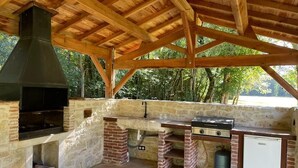An outdoor barbecue area with a stone wall, a grill, a chimney, and a small refrigerator.