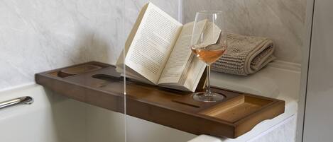 A bathroom with a wooden tray holding an open book and a glass of wine.