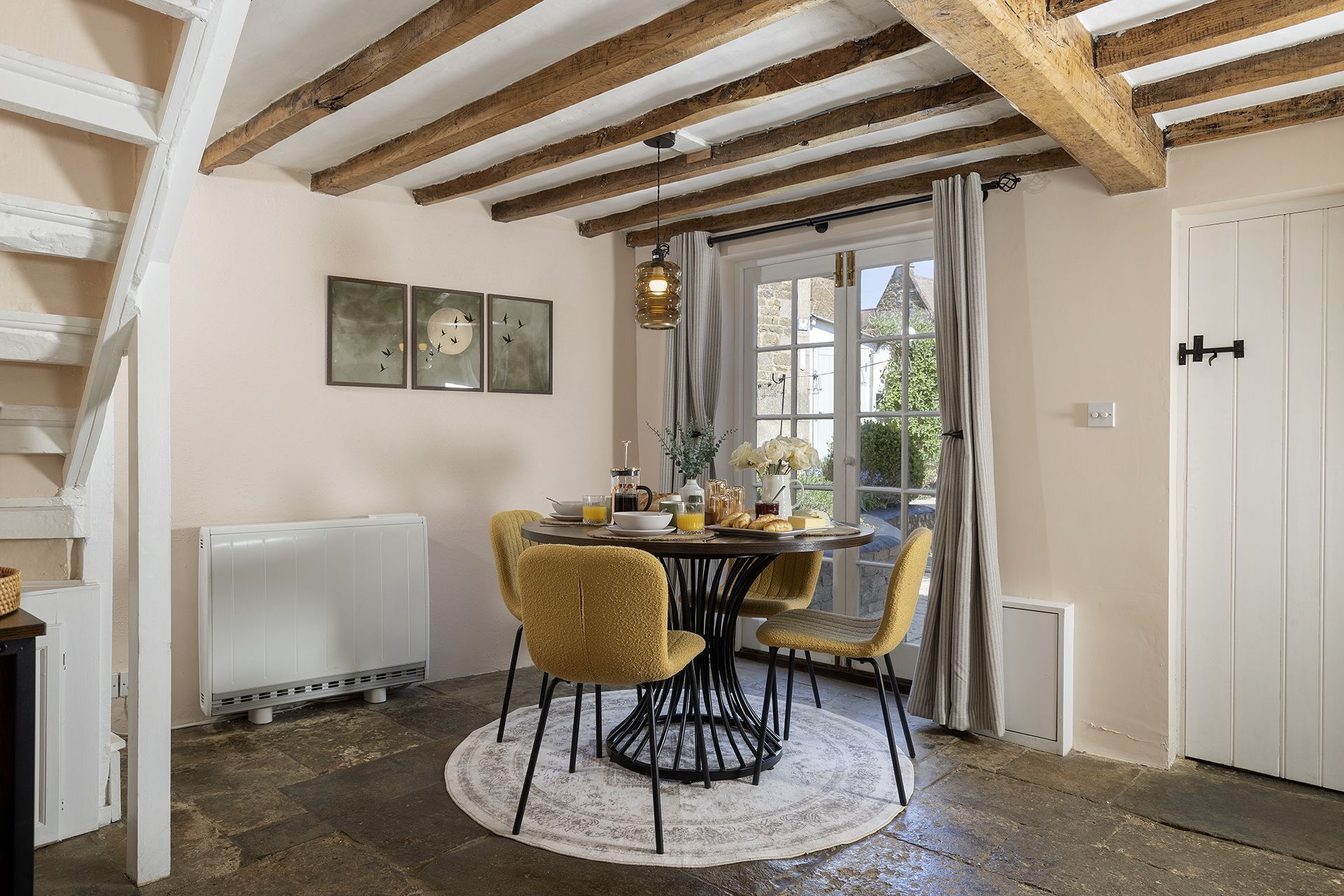 Un coin repas comprenant une table ronde, des chaises, un radiateur et une fenêtre avec des rideaux.