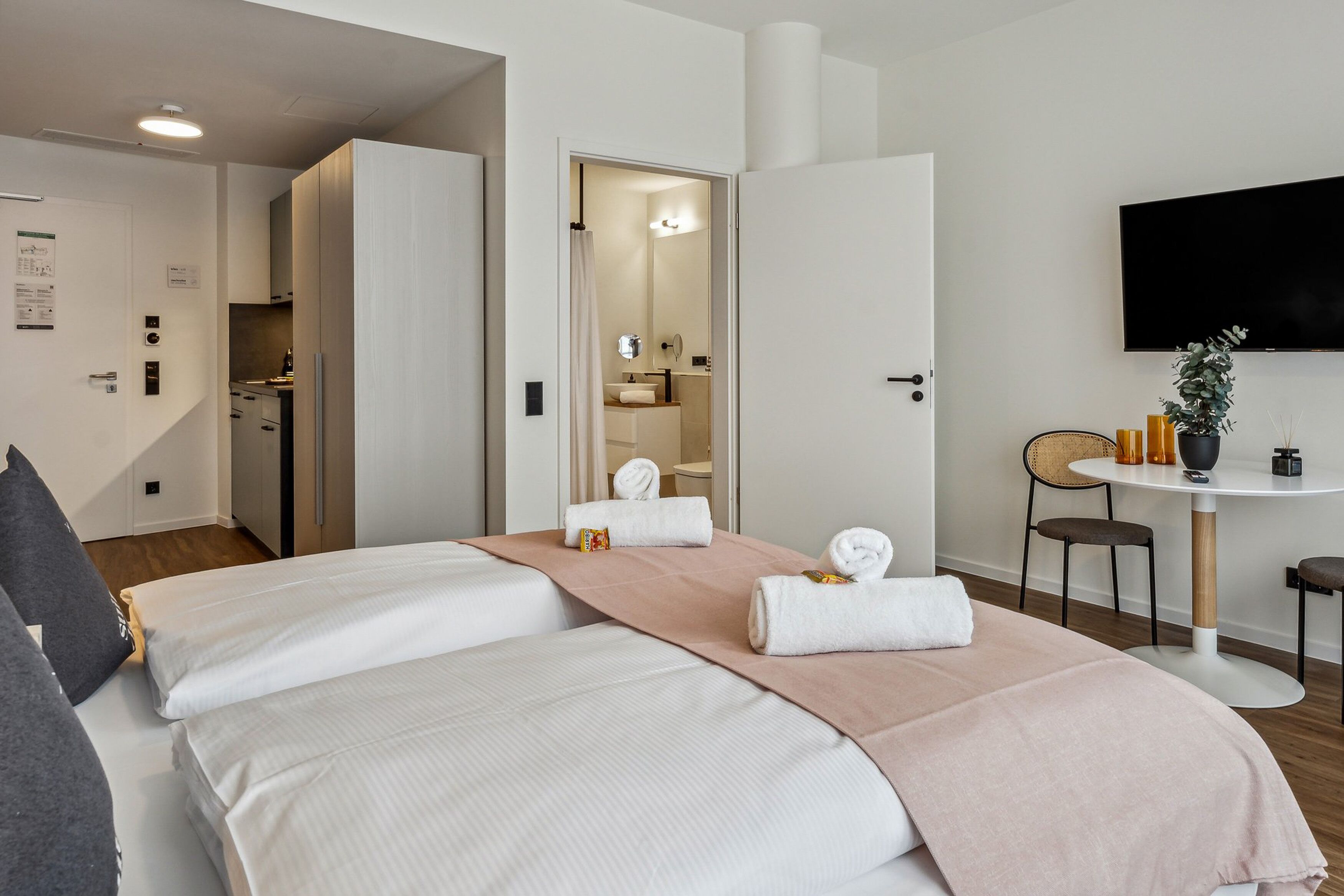 Camera d'albergo con due letti, un tavolo da pranzo, una TV e un bagno visibile attraverso una porta aperta.