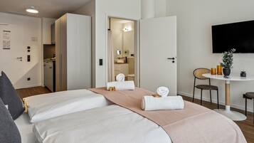 Camera d'albergo con due letti, un tavolo da pranzo, una TV e un bagno visibile attraverso una porta aperta.