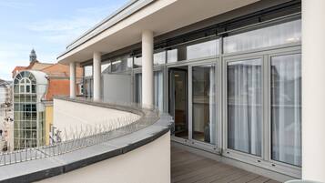 A balcony with a curved glass railing, large windows, and a view of the cityscape.