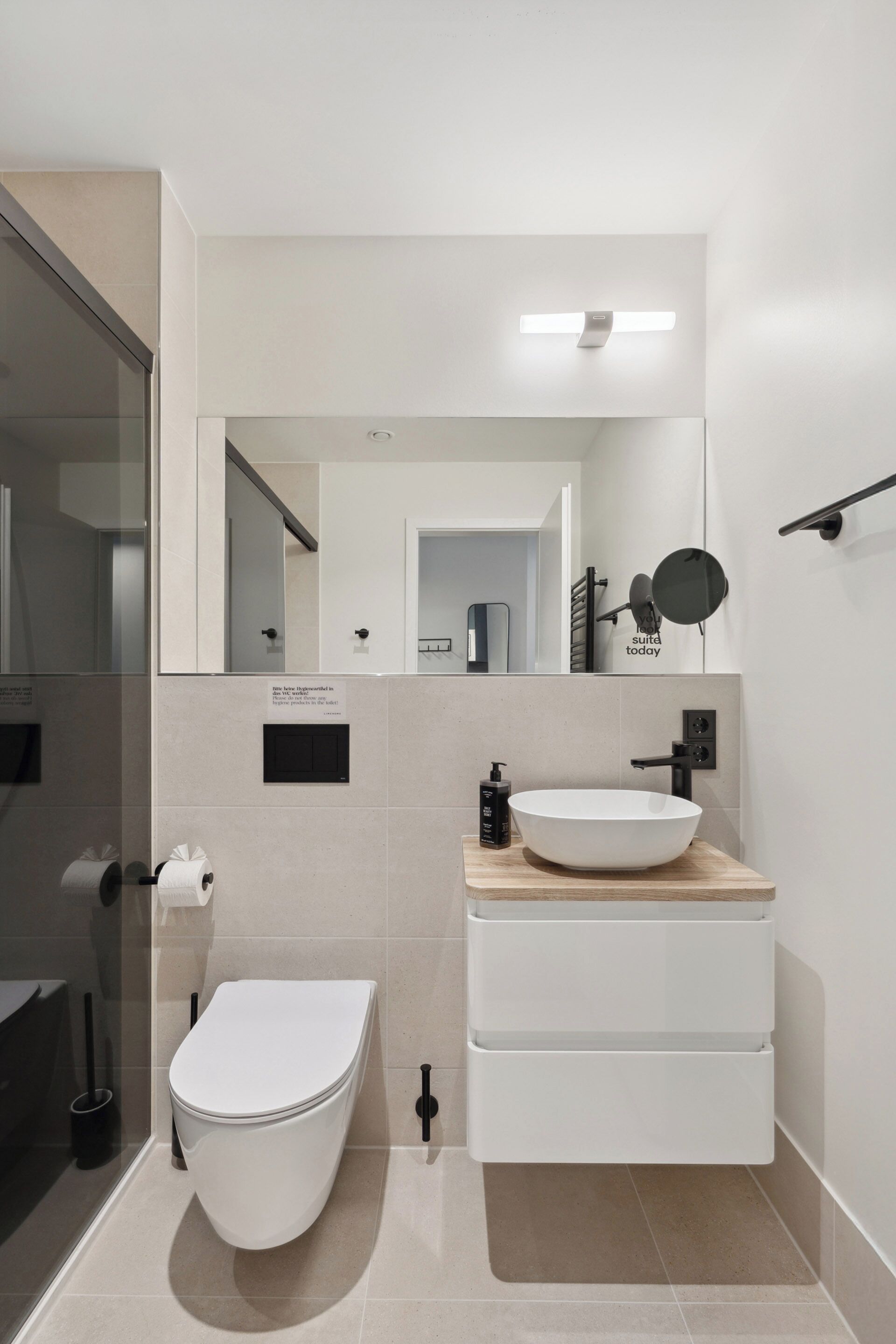 A modern bathroom with a white toilet, a wooden vanity with a white sink, and a mirror above the vanity.