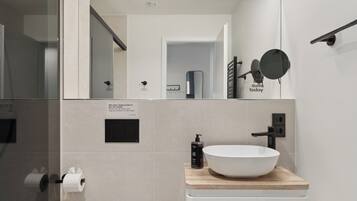 A modern bathroom with a white toilet, a wooden vanity with a white sink, and a mirror above the vanity.