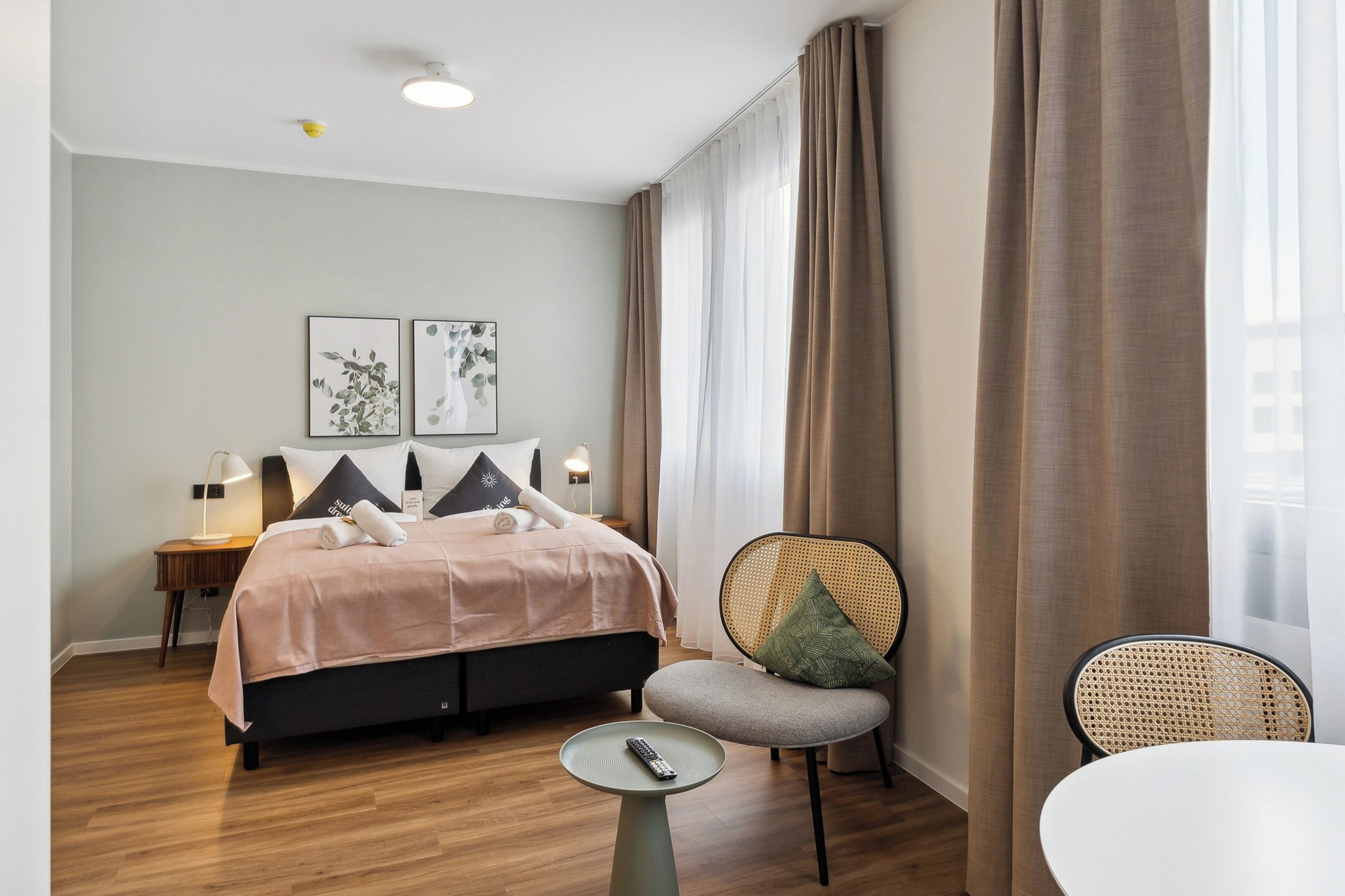 A modern hotel room with a bed, bedside tables, a chair, and a small table with a remote control.